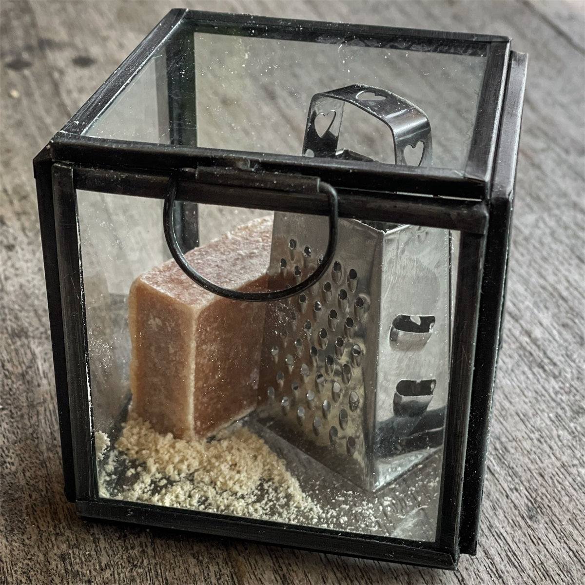Ein Glaskasten mit einer Raspel und einen braunen Duftblock 