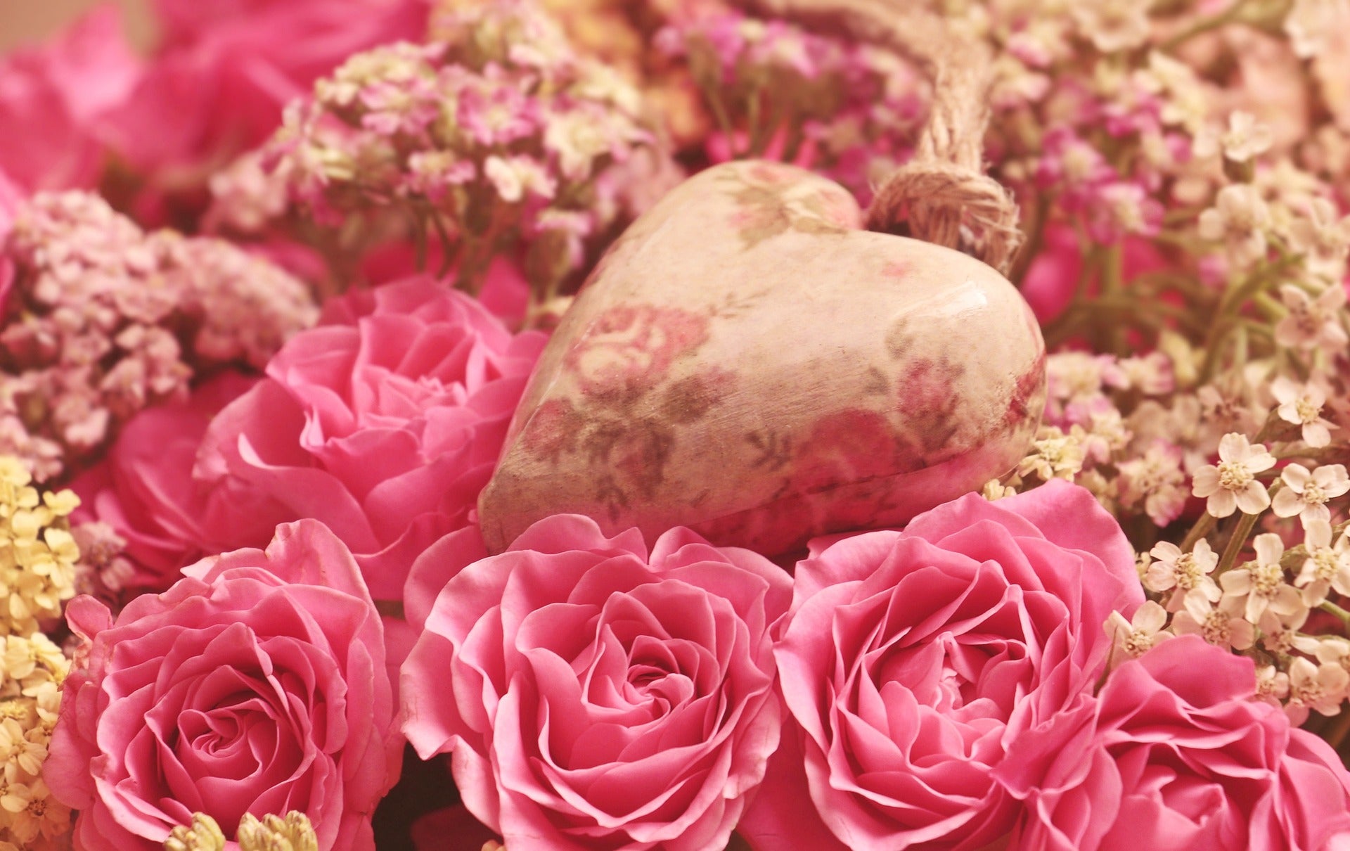 Viele rosafarbene Rosen und ein Stein der wie ein herz geformt ist 